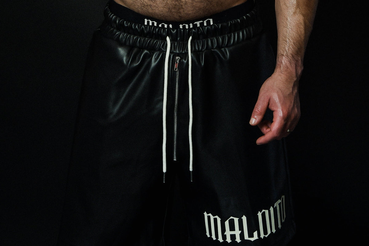 Close-up detail of the MALDITO black leather shorts showing the texture and construction.
