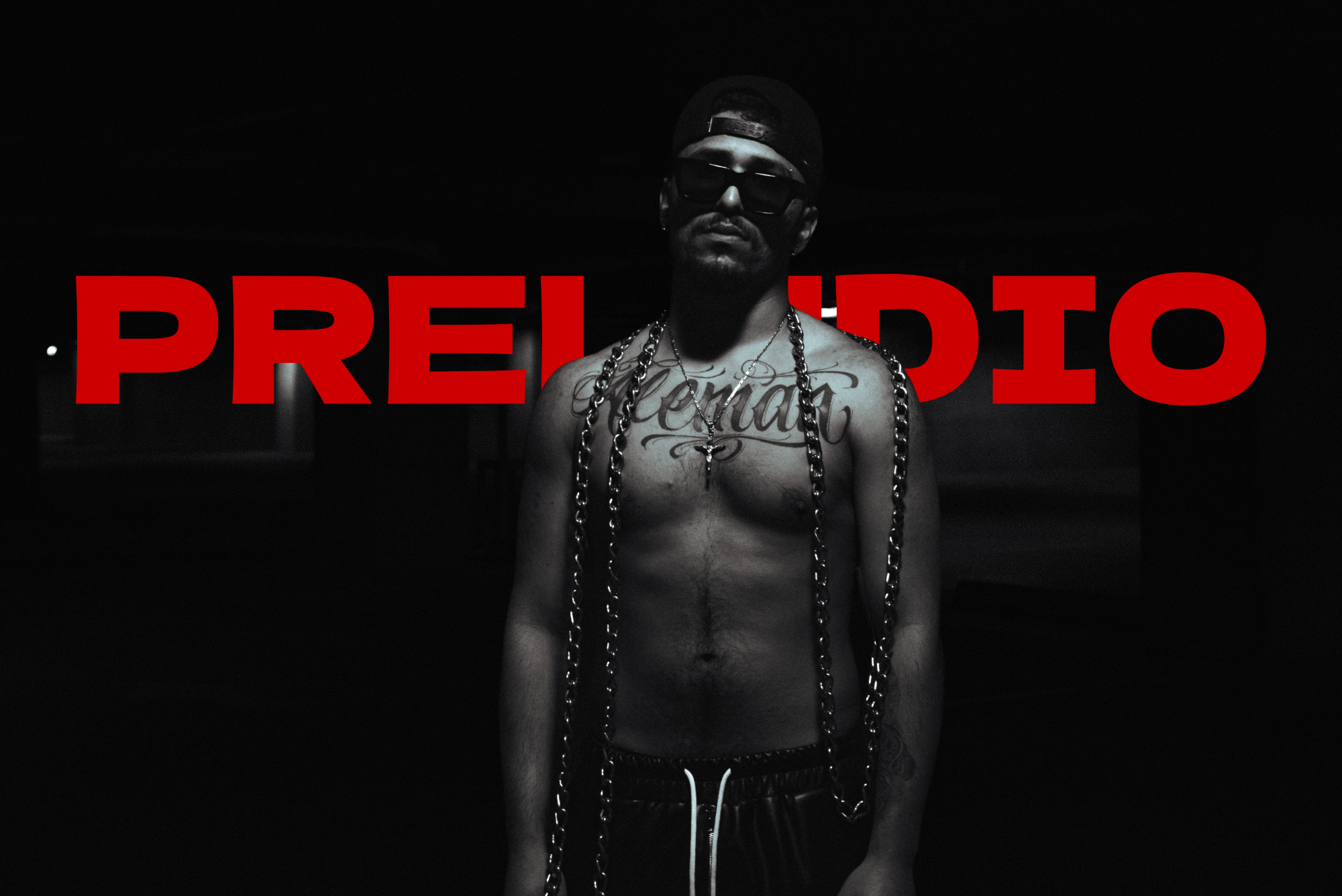Man with chains and tattoos in front of a black background with 'PRELUDIO' text.