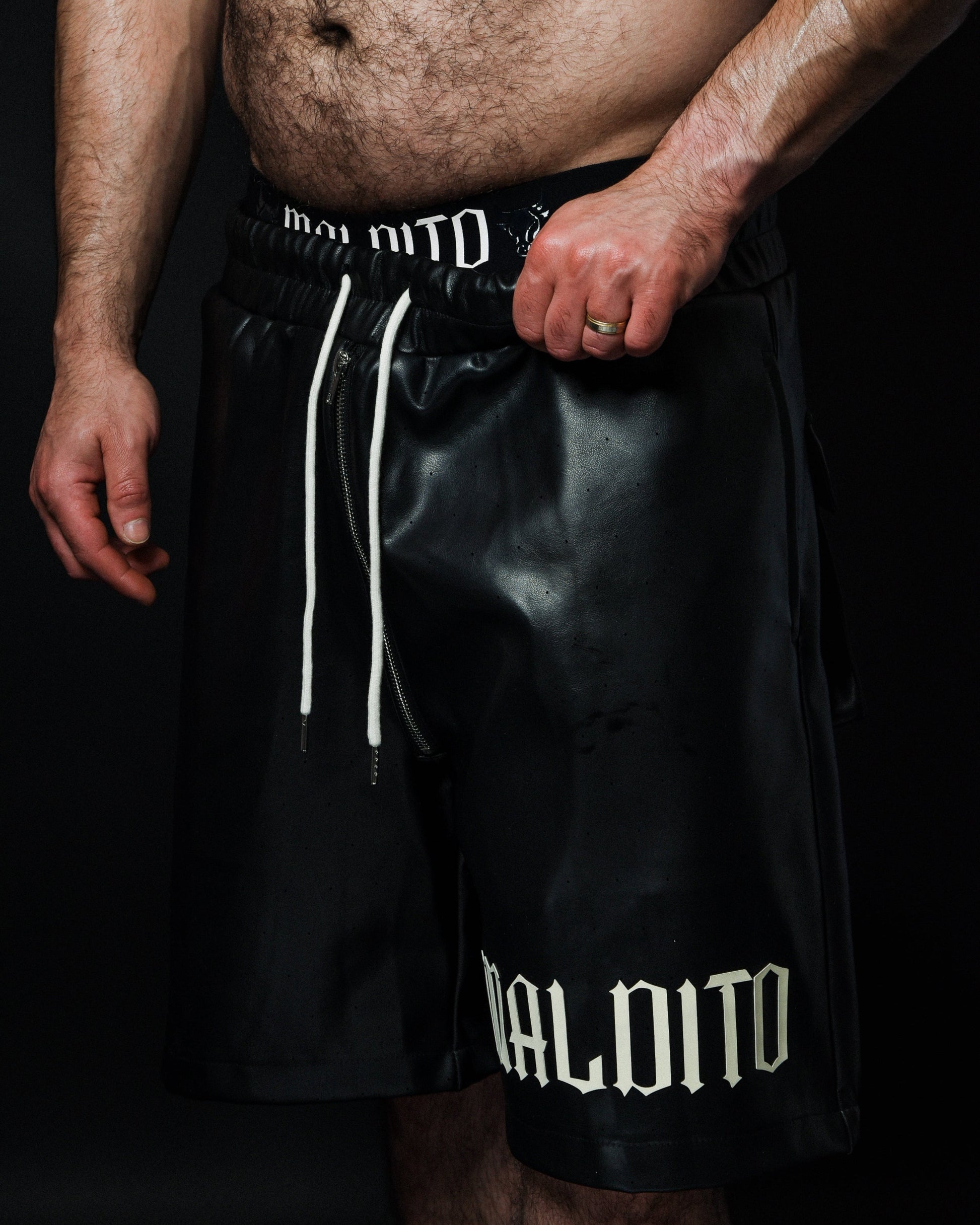 Angled view of model adjusting MALDITO Restraint leather shorts with extended drawstrings